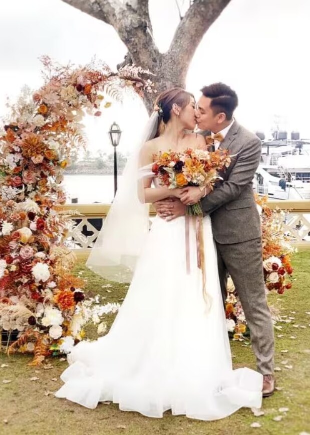 Picture of a bride and groom kissing at the altar among pink and white flowers